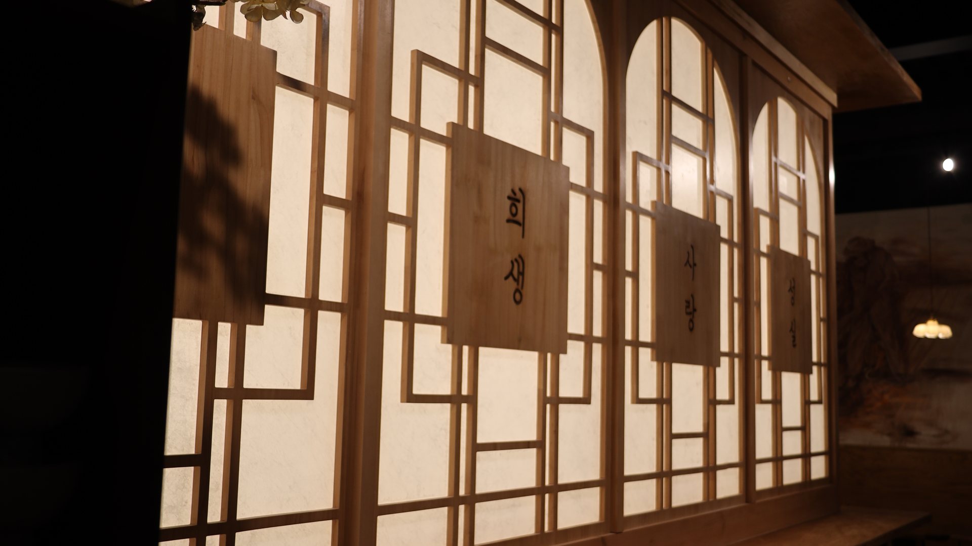 Backlit hanji lattice screens with carved Korean words at Rice Thief